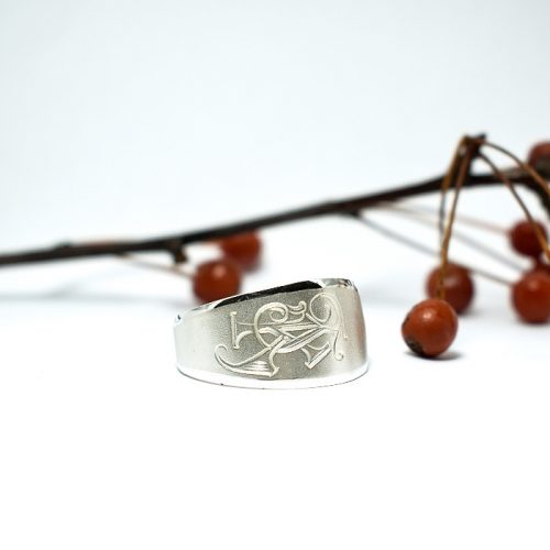 Monogrammi-sormus, joka on valmistettu hopealusikan varresta, sormuksen pintakuviossa on tyylitellyt nimikirjaimet.