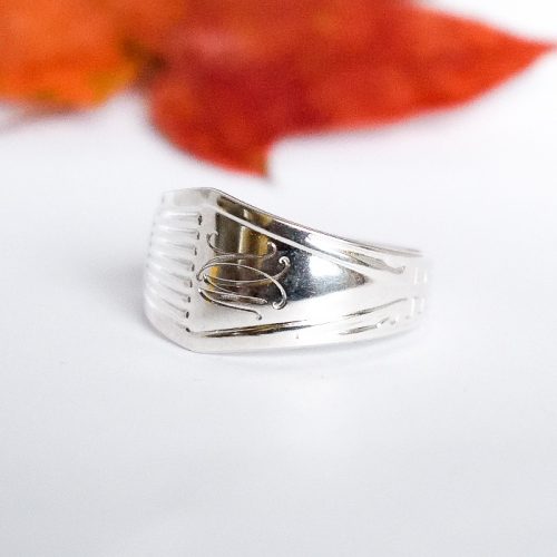 Suomi-hopeasormus, joka on muotoiltu Suomi-kahvilusikasta. Lusikka on vuodelta 1966 ja sormuksessa on koristeena monogrammikaiverrus.