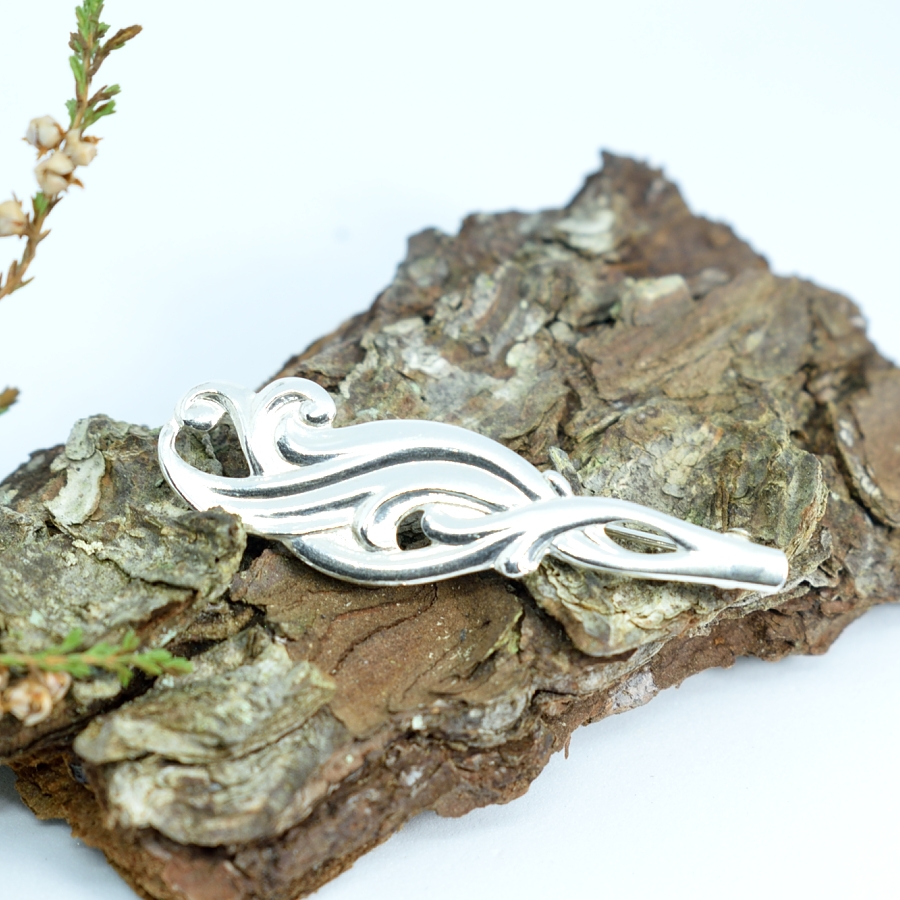 Kiekurat-rintaneula, joka on valmistettu hopealusikan varsiosasta. Lusikka on alun perin vuodelta 1951.