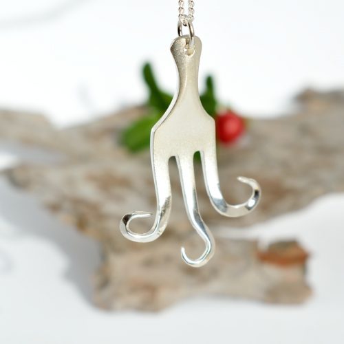 Mustekala-riipus, joka on muotoiltu hopeisesta leikkelehaarukasta. Korun pinta on käsitelty hieman huurteiseksi.