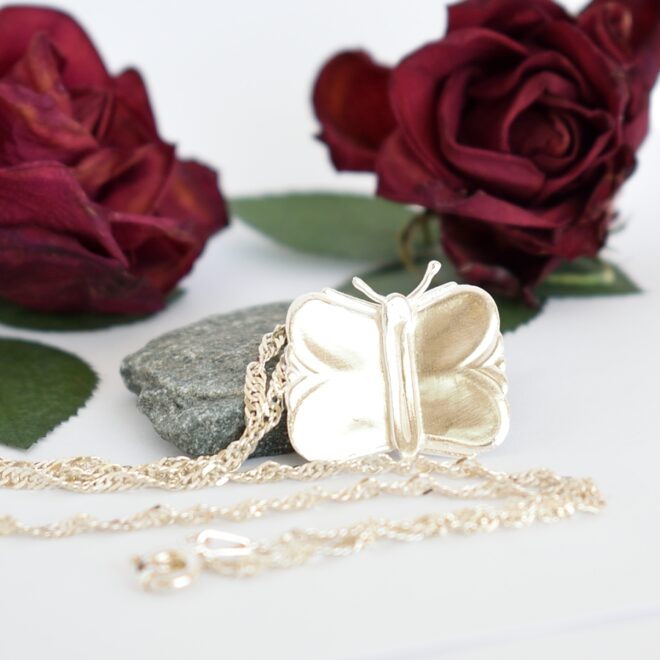 Perhonen-riipus, jonka siivet on muotoiltu kahden hopeisen jälkiruokalusikan varresta. Koruun on lisätty perhosen vartalo sekä tuntosarvet.